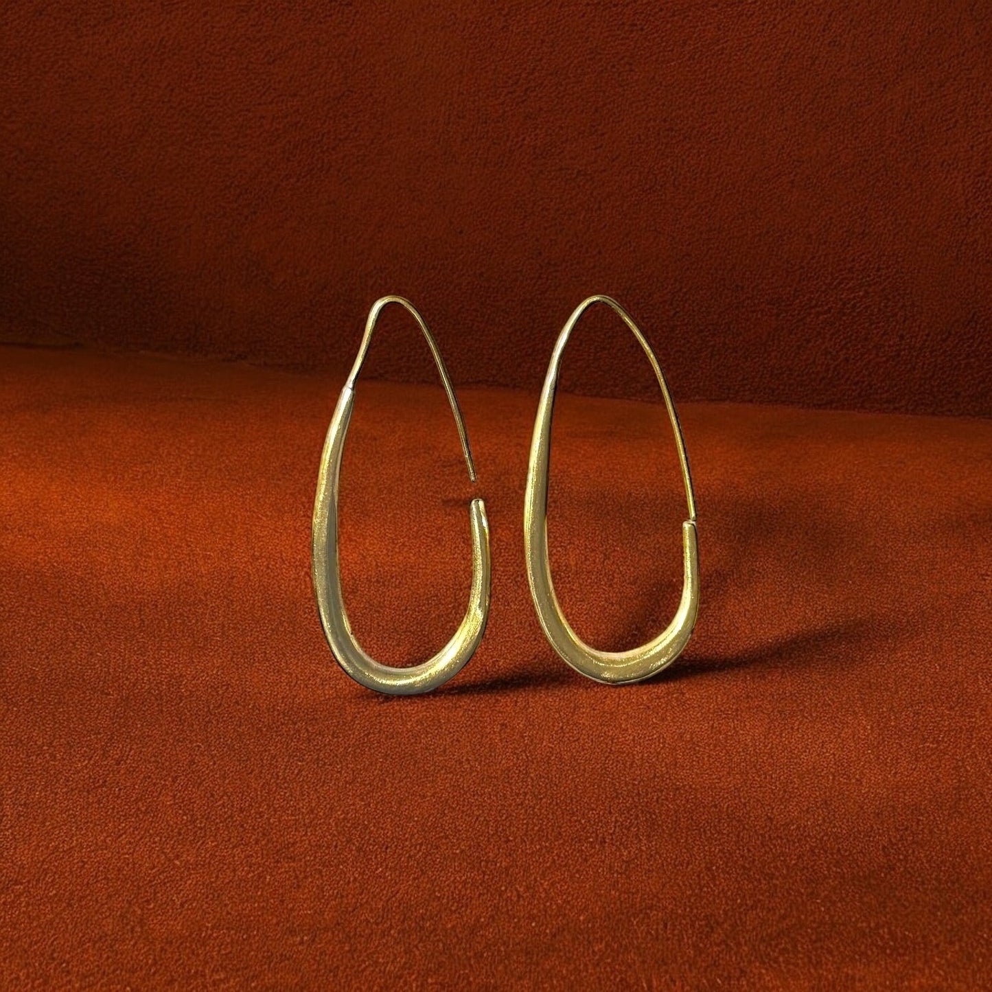 Gold hoop earrings on a rust-colored fabric background